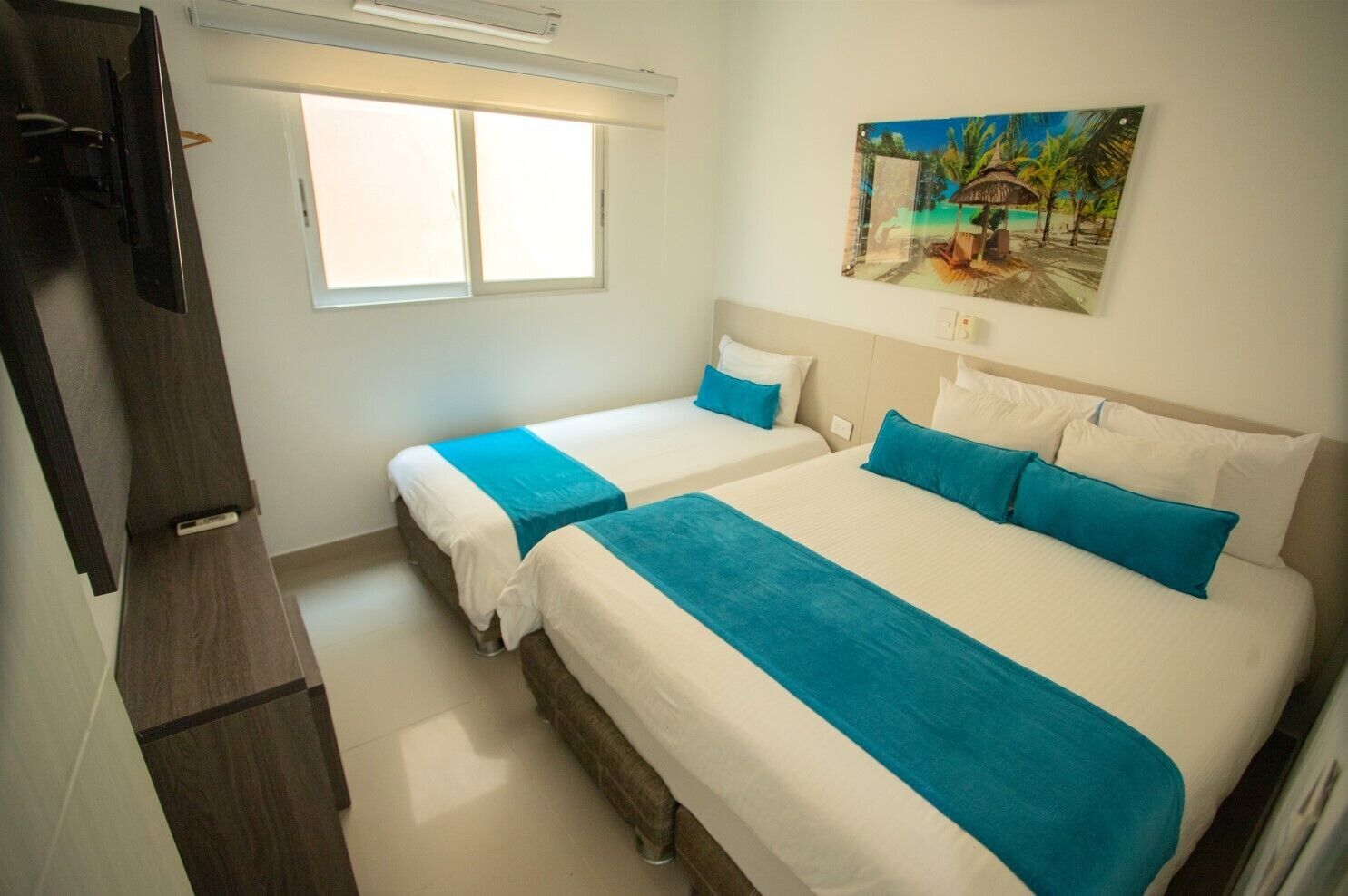 Habitación de hotel con dos camas, un ventanal grande y un cuadro de una playa.