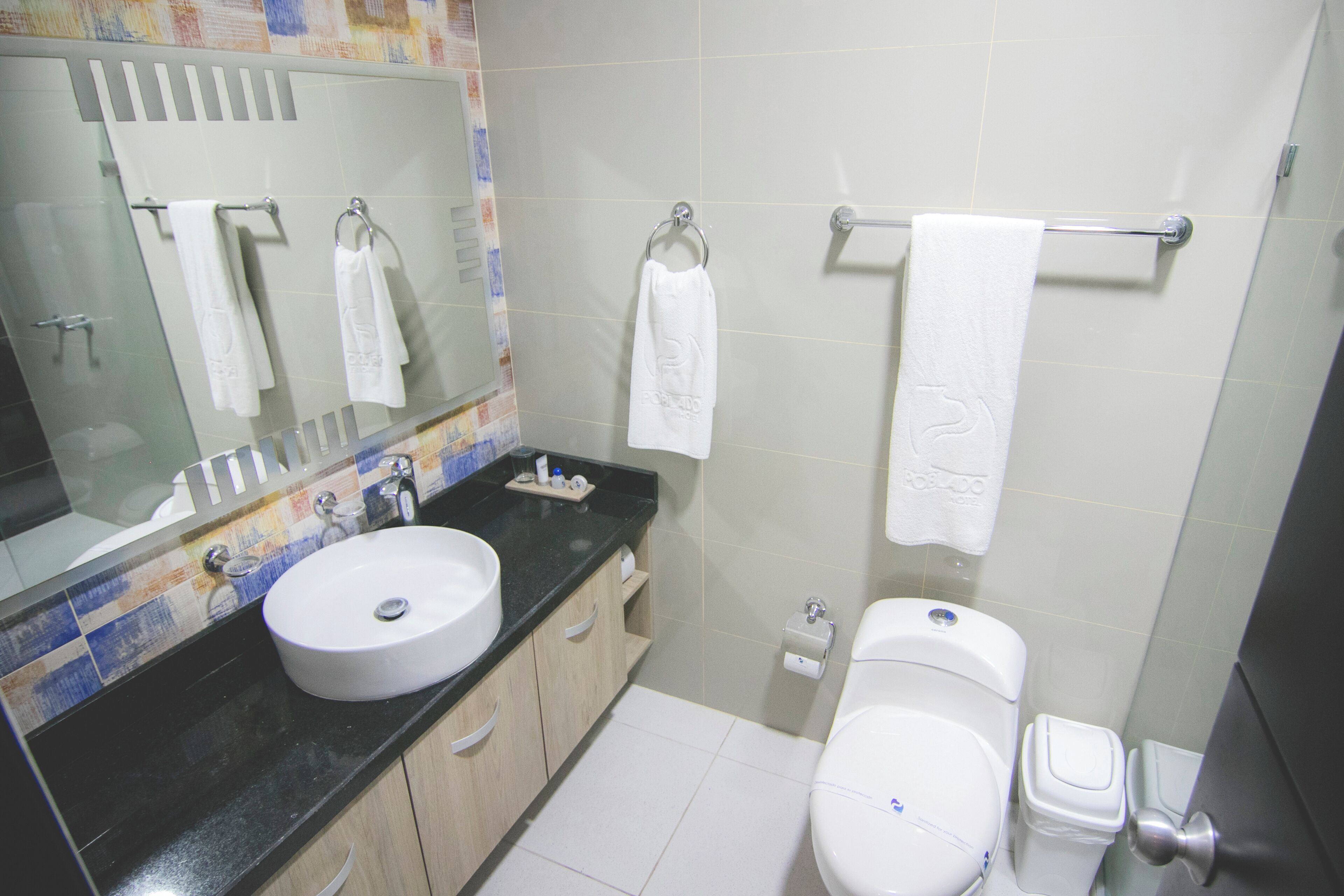 Un baño con lavamanos, espejo, inodoro y toallero.