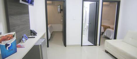 A hotel room with a reception desk, a television, a white sofa, and two doors leading to a bathroom and a bedroom.