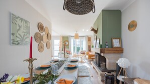 A dining area with a long table set for a meal, surrounded by chairs, a fireplace, and decorative wall art. - Ellisa - Jolie Maison proche de la mer (Ver-sur-Mer)