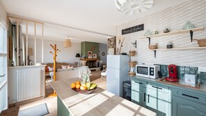 A modern kitchen with light blue cabinets, a wooden island with fruit, and a wall-mounted shelf with kitchenware. - Ellisa - Jolie Maison proche de la mer (Ver-sur-Mer)