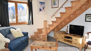 Un salon avec un canapé bleu, un escalier en bois et un téléviseur posé sur un meuble en bois.