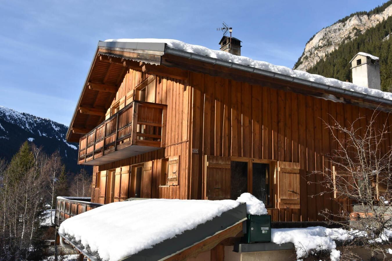 Un chalet en bois doté d’un balcon, entouré de montagnes enneigées.