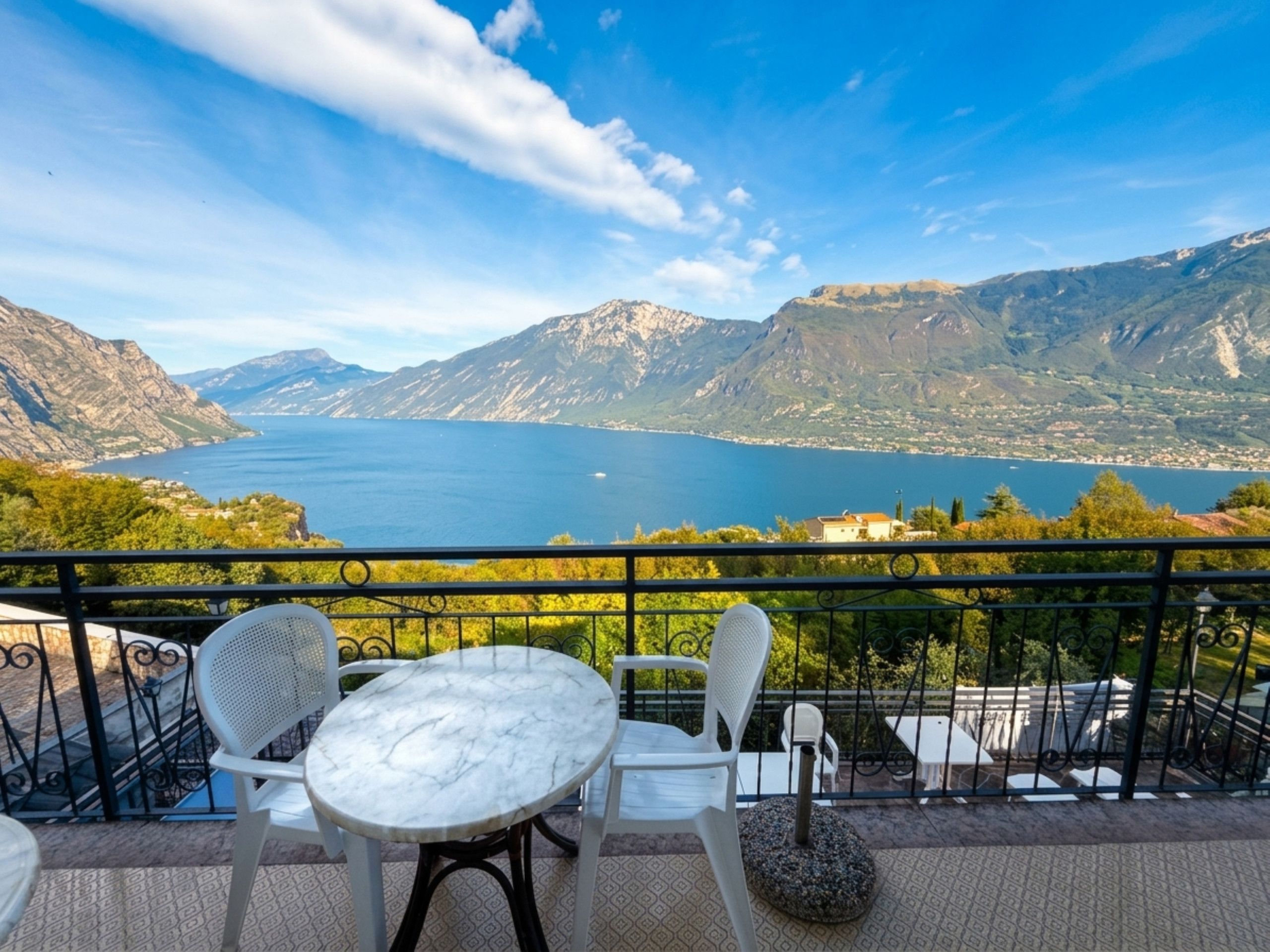 Terraço com mesa e cadeiras, vista para um lago e montanhas.