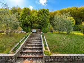 Un escalier en pierre mène à une zone abritée, entourée d’une végétation luxuriante et d’arbres.