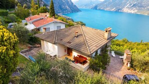 Una casa con techo de tejas, un patio con mobiliario exterior y vistas a un lago y montañas.