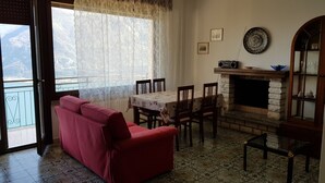 Una sala de estar con un sofá rojo, una mesa de comedor con sillas, una chimenea y vistas al exterior.