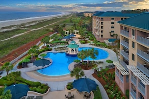 Relax by the resort's central pool surrounded by lush landscaping and palm trees, with a scenic ocean view.