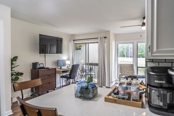 A modern kitchen with a dining area, a flat-screen TV, and a coffee maker. - To The Green On #17 - Boutique Studio w/ GREAT Views, 5 Minutes From Clubhouse (Pinehurst)