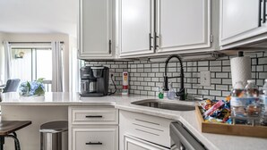 A kitchen with white cabinets, a coffee maker, a sink, and a trash can. - To The Green On #17 - Boutique Studio w/ GREAT Views, 5 Minutes From Clubhouse (Pinehurst)