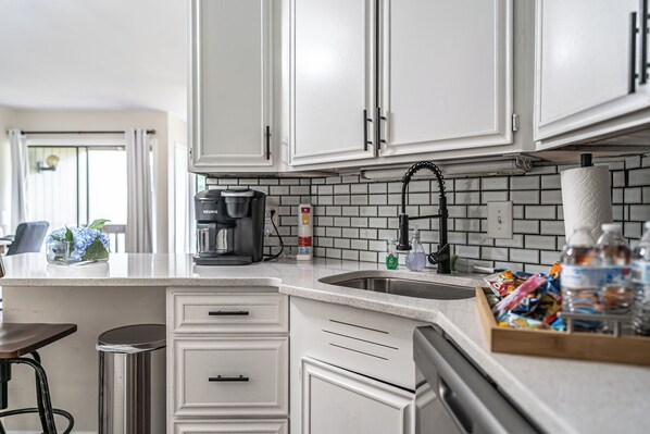 A kitchen with white cabinets, a coffee maker, a sink, and a trash can.