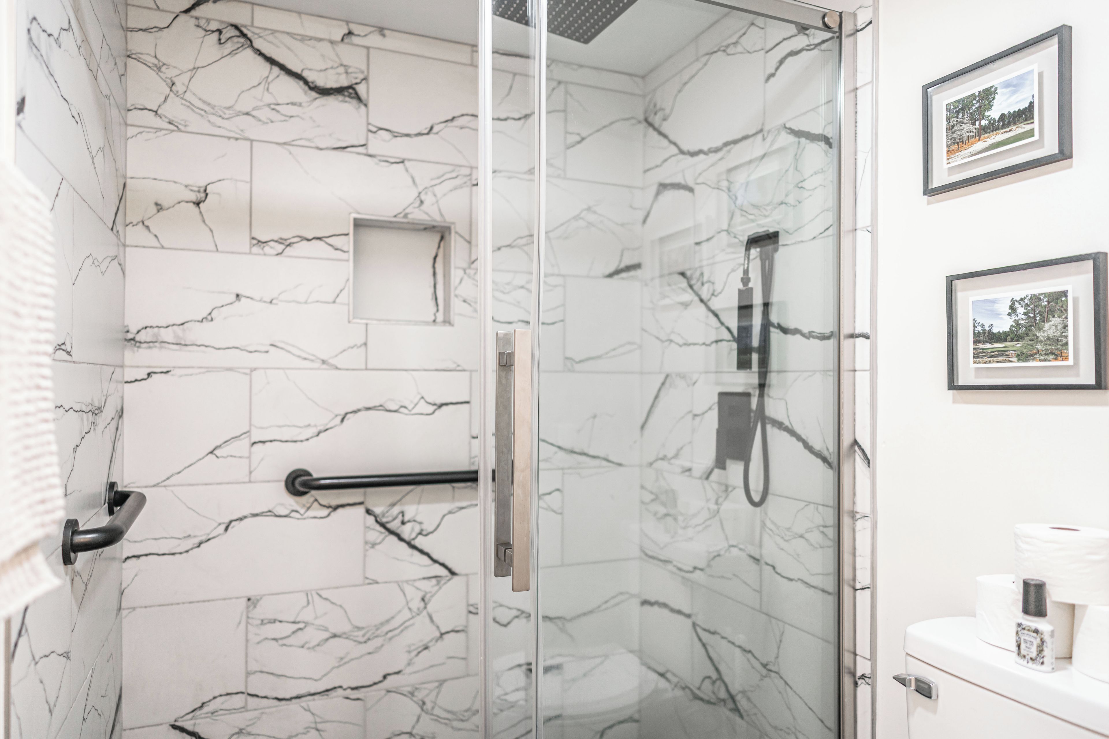 A bathroom with marble walls, a glass shower enclosure, a towel rack, and framed pictures on the wall.