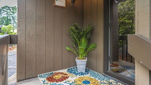 A wooden exterior wall with a potted plant, a framed sign, and a patterned mat at the entrance. - To The Green On #17 - Boutique Studio w/ GREAT Views, 5 Minutes From Clubhouse (Pinehurst)
