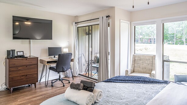 A hotel room with a bed, a desk with a computer, a TV, a chair, and a view of the outdoors. - To The Green On #17 - Boutique Studio w/ GREAT Views, 5 Minutes From Clubhouse (Pinehurst)