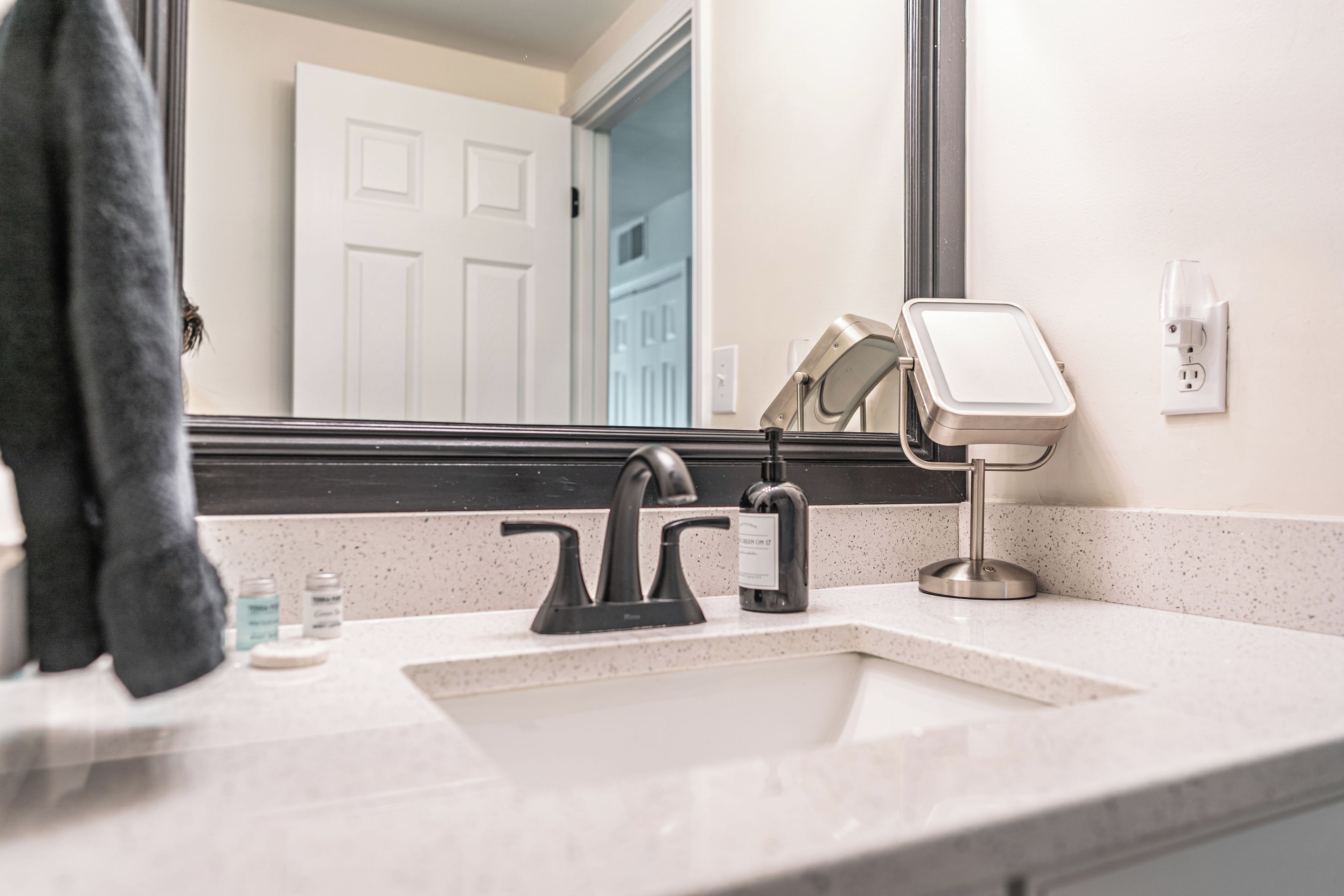 A bathroom with a white sink, black faucet, and a mirror with a light.