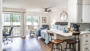 A modern bedroom with a large bed, a desk, and a chair. There is a balcony with a view of trees. - To The Green On #17 - Boutique Studio w/ GREAT Views, 5 Minutes From Clubhouse (Pinehurst)