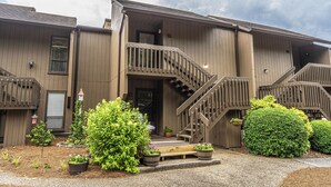 A building with a wooden exterior, a staircase leading to a balcony, and potted plants in the front yard.