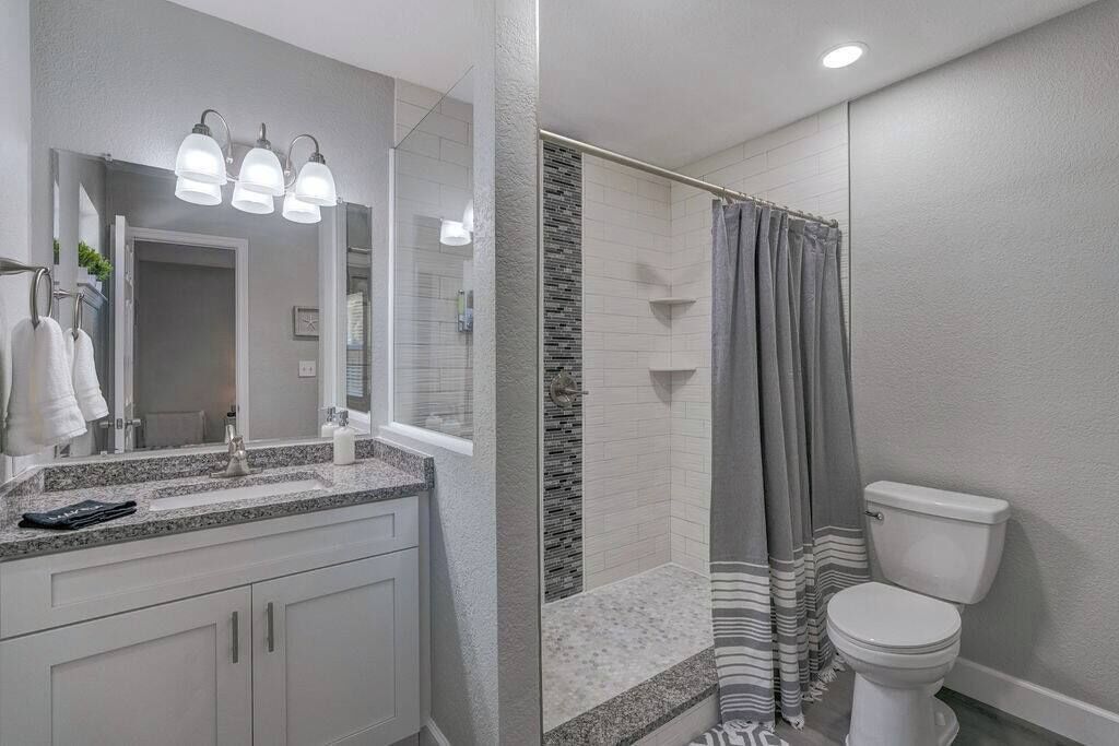 A modern bathroom with a granite countertop, a large mirror, and a shower with a striped curtain.