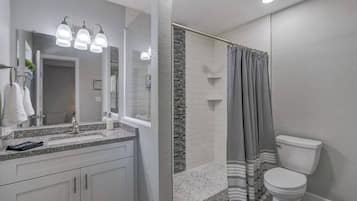 A modern bathroom with a granite countertop, a large mirror, and a shower with a striped curtain.