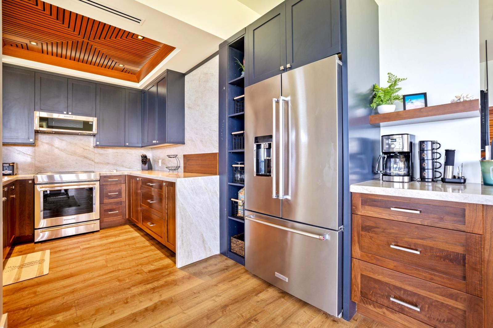A modern kitchen with dark cabinets, stainless steel appliances, and a wooden ceiling.