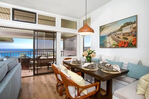 A dining area with a wooden table set for four, a sofa, and a painting of a coastal scene.