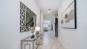 A hallway with a glass console table, a geometric mirror, and a framed abstract painting.