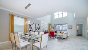 A spacious dining area with a glass table, white chairs, and yellow curtains.