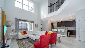 A spacious living area with a white sofa, red chairs, and a coffee table. A kitchen is visible in the background with dark cabinets and a microwave.