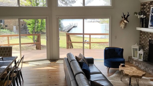 A spacious living room with a large window, a leather sofa, a blue armchair, and a fireplace. - Lake Murray Gem - Lakefront Dock (Chapin)