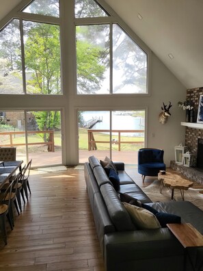 A spacious living room with a large window, a leather sofa, a blue armchair, and a fireplace.