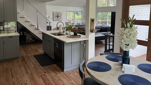 A modern kitchen with a central island, a dining area with a round table, and a staircase leading to an upper level. - Lake Murray Gem - Lakefront Dock (Chapin)