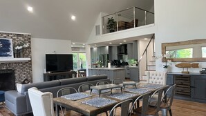 A spacious living area with a large TV, grey sofa, dining table with placemats, and a kitchen in the background. - Lake Murray Gem - Lakefront Dock (Chapin)