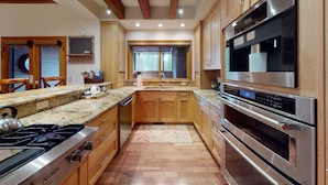 A modern kitchen with wooden cabinets, granite countertops, a stainless steel stove, and a large window.