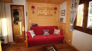 En hyggelig stue med en rød sofa, trævægge og et vindue med mønstrede gardiner.