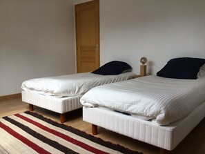 Two single beds with white bedding and dark pillows, a wooden door, and a striped rug. - Bright house near the sea (Névez)