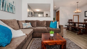 Una sala de estar moderna con un sofá seccional marrón, una mesa de centro de madera y un comedor con una mesa y sillas de madera.
