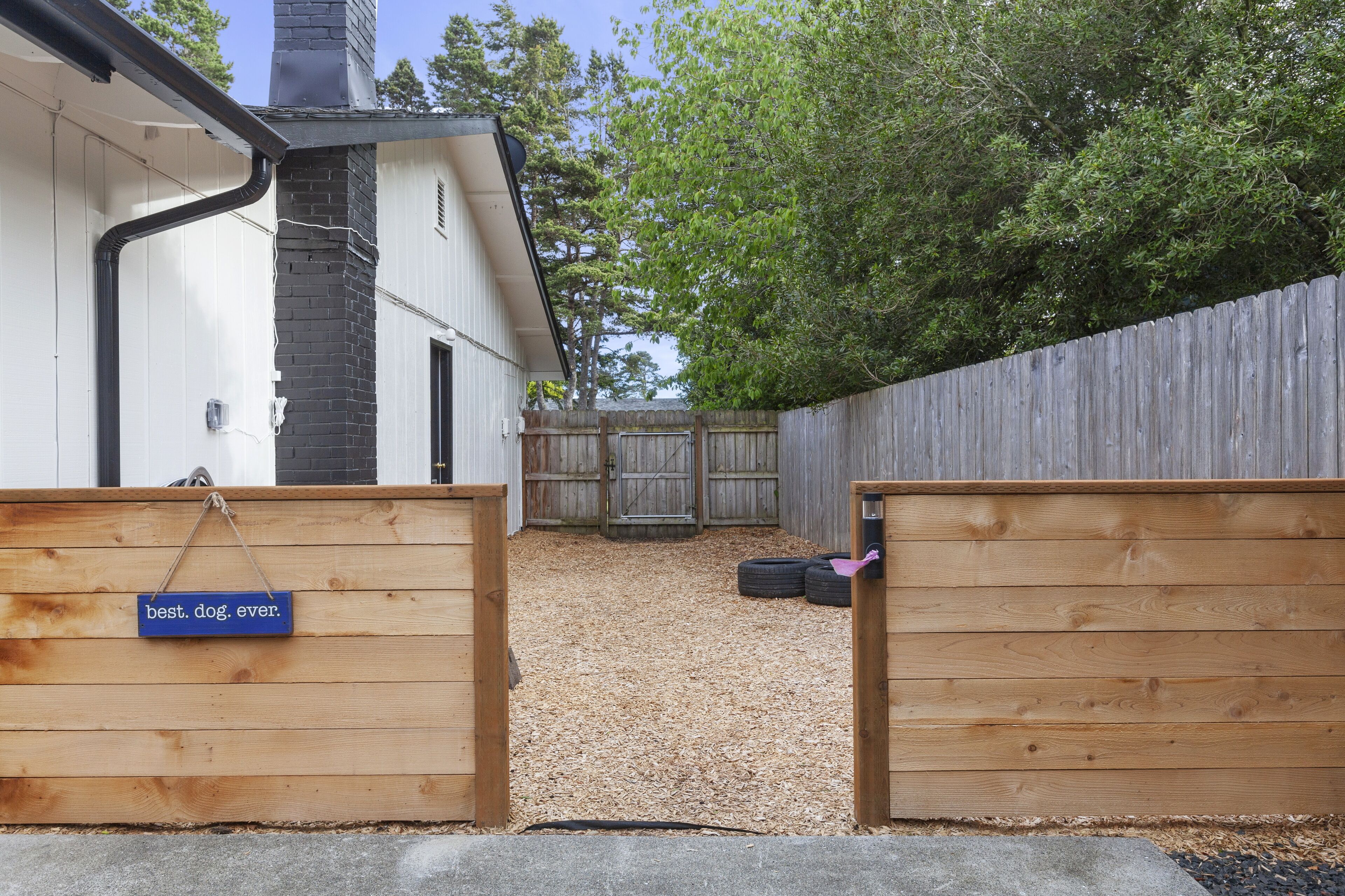 A backyard with a wooden fence, a dog gate, and a gravel path leading to a wooden deck.