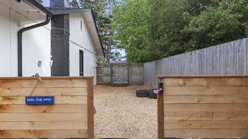 A backyard with a wooden fence, a dog gate, and a gravel path leading to a wooden deck.