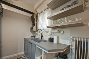 A compact kitchen with a built-in sink, wooden shelves above the countertop, and a radiator below. - Stylish Apartment at Pagrati (Vironas)