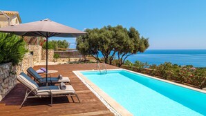 A wooden deck with lounge chairs and an umbrella, a swimming pool, and a view of the sea. - The Yiameli Collection - Yasmi (Micro Nisi)