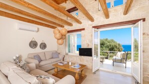 A cozy living room with a sofa, coffee table, and a view of the sea through an open door. - The Yiameli Collection - Yasmi (Micro Nisi)