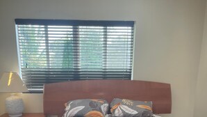 Une chambre à coucher avec un lit, une table de chevet, une lampe et une fenêtre avec des stores.