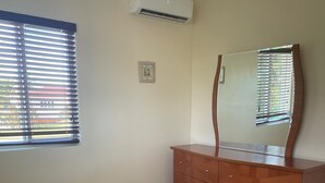 Une chambre à coucher comprenant un lit, une commode, un miroir et une fenêtre avec des stores.