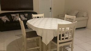 Un coin repas avec une table ronde, quatre chaises, un ventilateur de plafond, une porte, une fenêtre avec des stores et un canapé à rayures.
