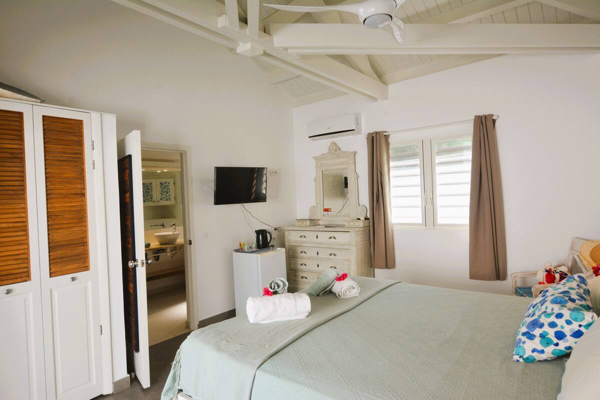 Ein Hotelzimmer mit Bett, Fernseher, Schminktisch, Spiegel und einem durchgegangenen Tür sichtbaren Badezimmer.
