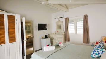 Une chambre d’hôtel avec un lit, une télévision, une commode, un miroir et une salle de bain visible à travers une porte ouverte.