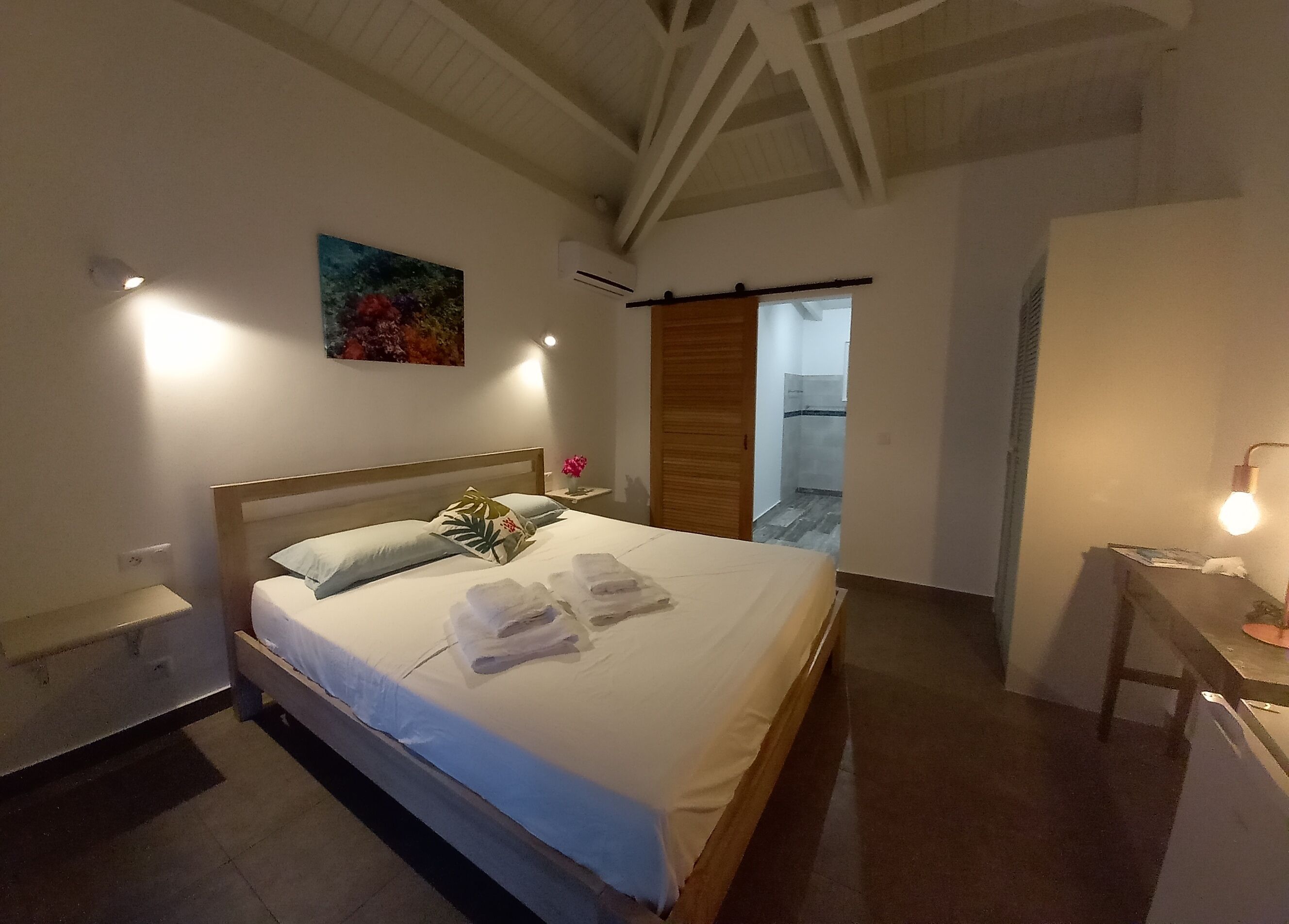 Une chambre à coucher comprenant un lit, une table de chevet et une commode. Une porte donne accès à la salle de bain.