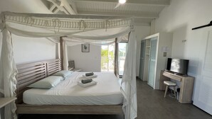 Un dormitorio con cama con dosel, ventilador de techo, televisor y escritorio.