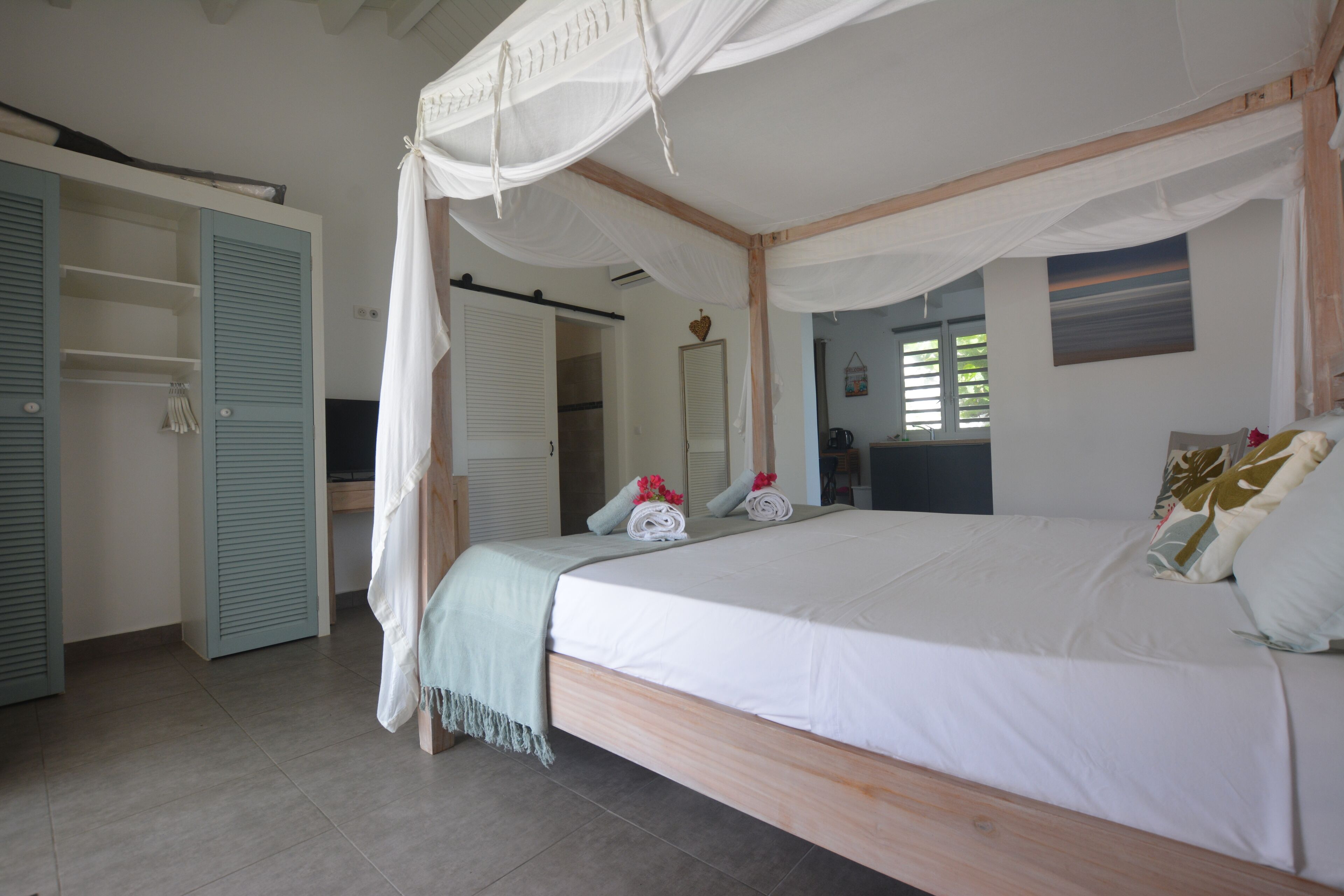A bedroom with a canopy bed, a wardrobe with blue shutters, and a mirror on the wall.