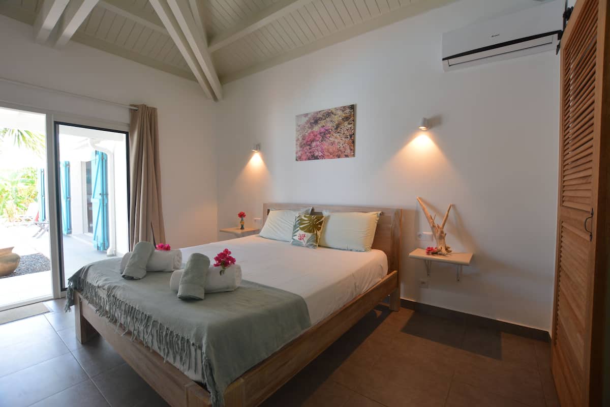 Ein Schlafzimmer mit Bett, Nachttisch, Klimaanlage und Blick ins Freie.